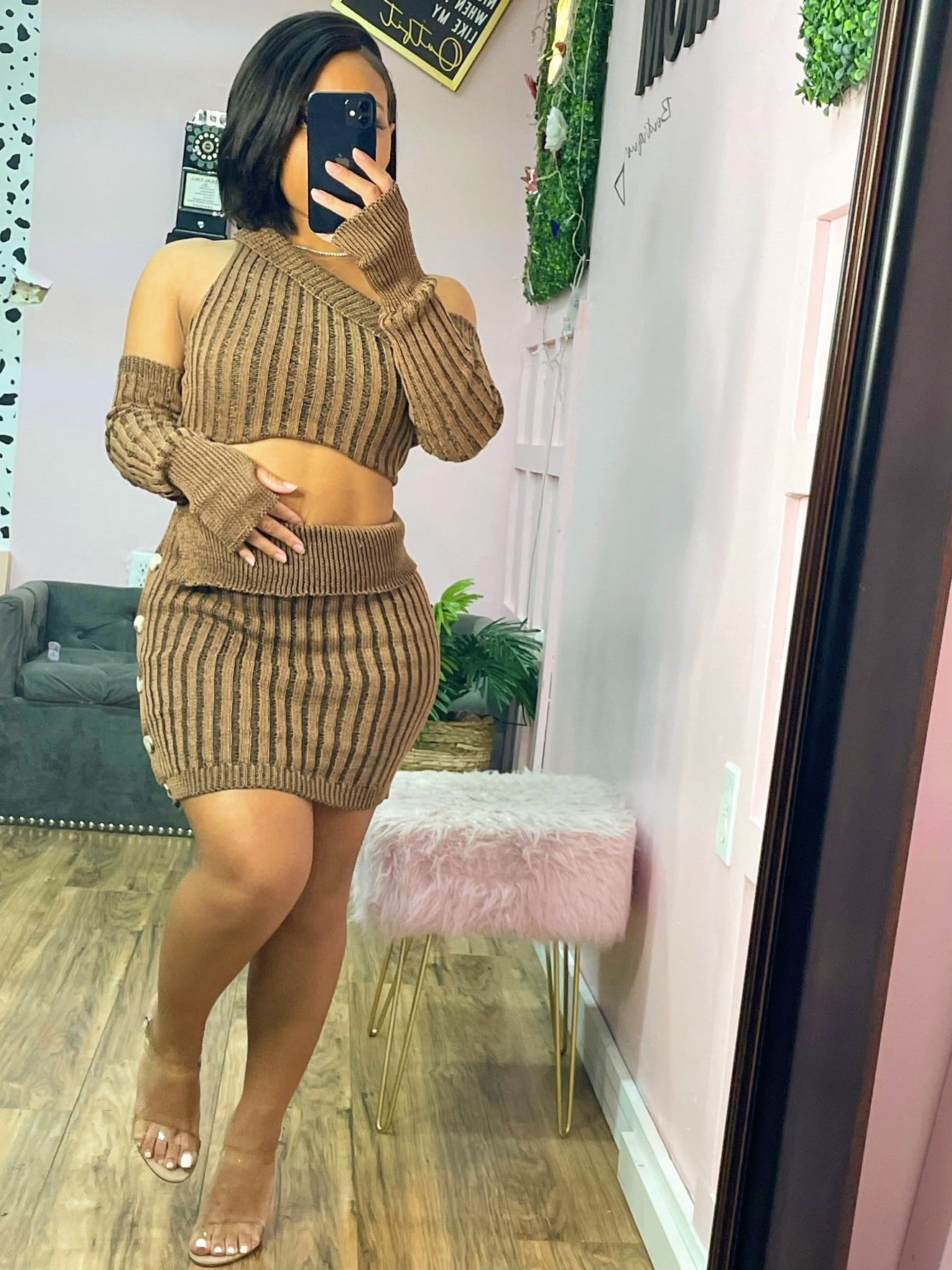 Person wearing a brown ribbed outfit taking a mirror selfie in a room with pink walls and decor.